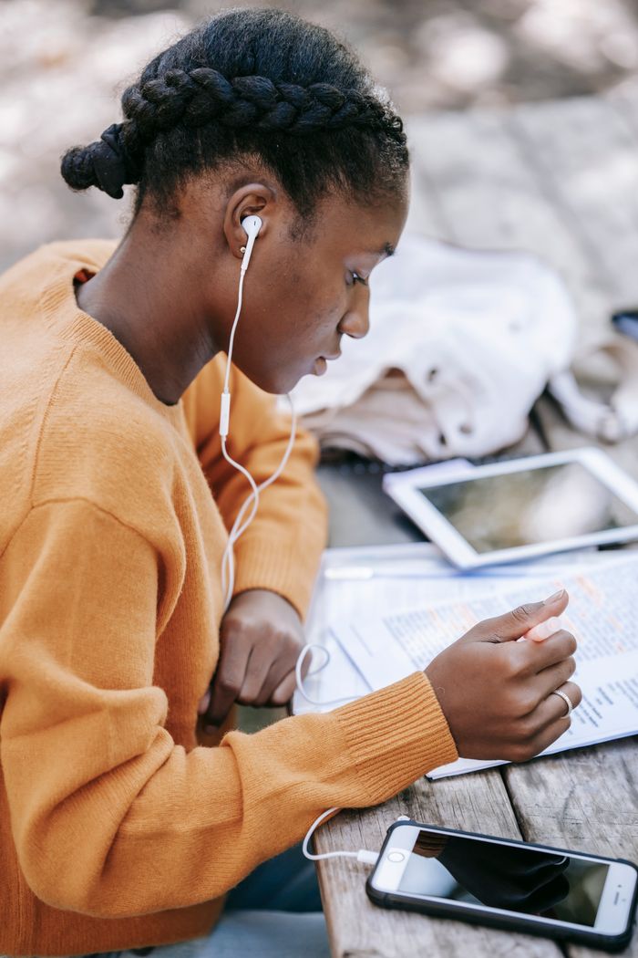 services-02 Side view of serious young African American female in earphones learning information while studying at table with mobile phone